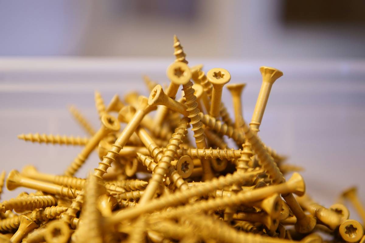 Assortment of small screws for wood laid on a cedar board, showing different head types and lengths